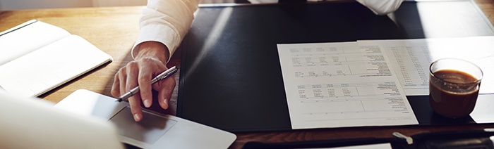 Teaser: Person die Notizen macht mit Laptop und Kaffee, Fokus auf Hände und Schreibtisch