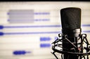 Sie sehen eine Fotografie zum Thema Podcast. Zu sehen ist ein Mikrofon vor einem Computerbildschirm