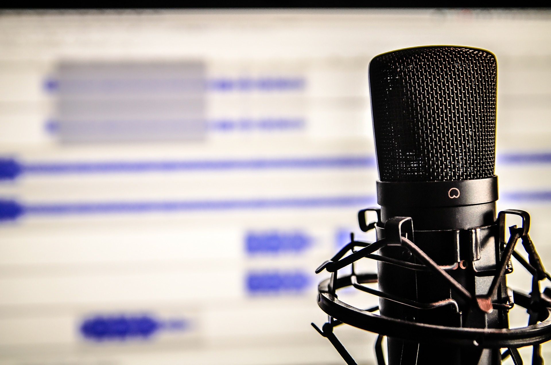 Sie sehen eine Fotografie zum Thema Podcast. Zu sehen ist ein Mikrofon vor einem Computerbildschirm