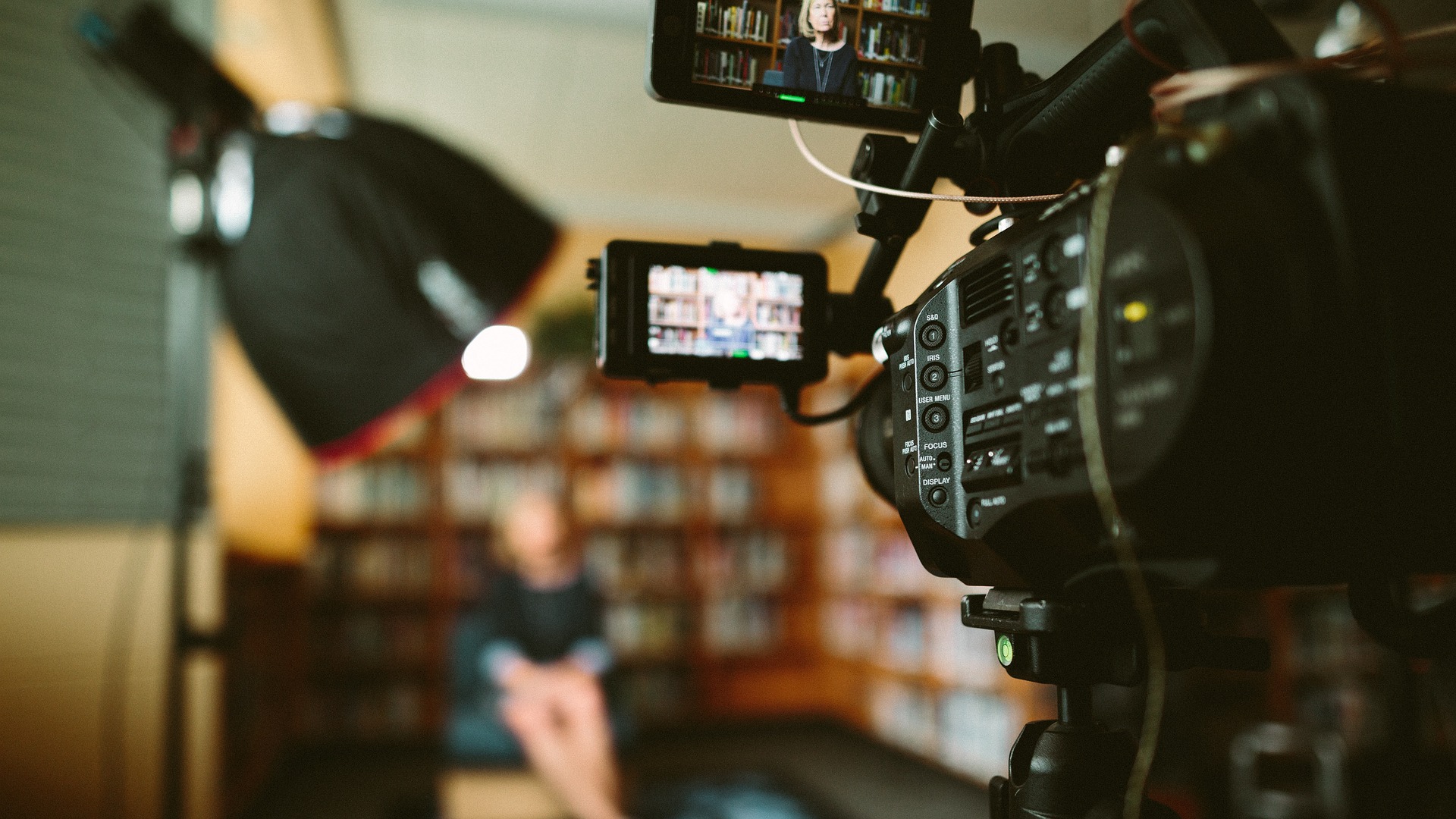 Sie sehen eine Fotografie zum Thema Videocast. Zu sehen ist eine Videokamera, die eine Person fokussiert.