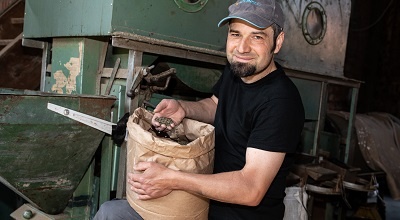 Man with a bag full of grain in front of a mill