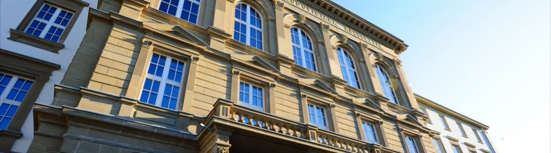 Slider: Fotografie des JLU-Hauptgebäudes mit blauem Himmel und Sonne (Bildbeschreibung und Bildnachweis siehe Quellenverzeichnis) / Slider: Photography of the university’s main building front of blue sky and sunshine