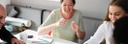 Slider: lachende Frau an Tisch mit Gruppe von Menschen, die sich unterhalten (Bildbeschreibung und Bildnachweis siehe Quellenverzeichnis) / Slider: laughing woman on a table, talking with a group of people