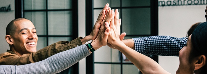 Bild: Lachende Menschen, deren sich abklatschende Hände im Fokus stehen // Photo: People laughing with the focus on their hands as they give each other high fives