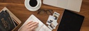 Bild: Banner der einen Schreibtisch mit Kaffee, Terminkalender und Laptop zeigt // Photo: Banner showing a wooden desk with a mug of coffee, a diary and a laptop on it