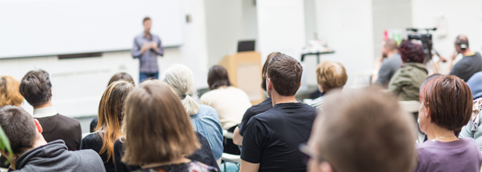 Bild: Lehrender vor einem Auditorium // Photo: Lecturer in front of a auditory