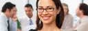 Bild: Lächelnde Frau mit Brille, im Hintergrund eine Gruppe im Gespräch // Photo: Smiling woman with glasses, in the background a group in conversation