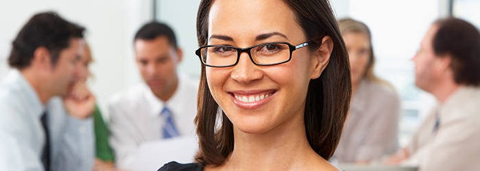 Bild: Lächelnde Frau mit Brille, im Hintergrund eine Gruppe im Gespräch // Photo: Smiling woman with glasses, in the background a group in conversation