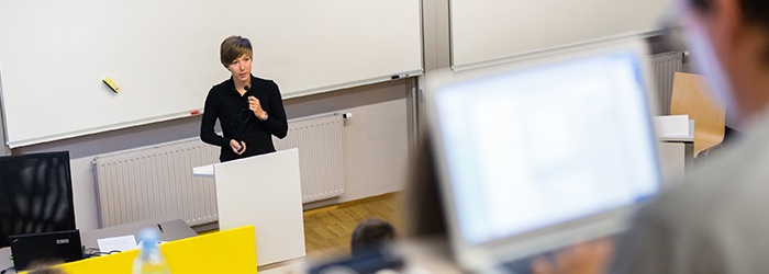Bild: Frau an Pult im Hörsaal // Photo: Woman at a desk in a lecture hall