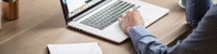 Bild: Ausschnitt einer Person an einem Schreibtisch mit Laptop // Photo: Detail of a person with a laptop at a desk