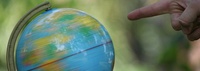 Bild: Hand, die auf einen sich drehenden Globus zeigt // Photo: Hand pointing to a spinning globe