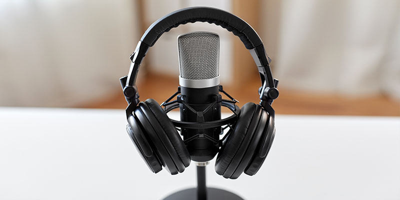 Kopfhörer klemmen an einem Tischmikrofon, Link auf Unterseite Podcast