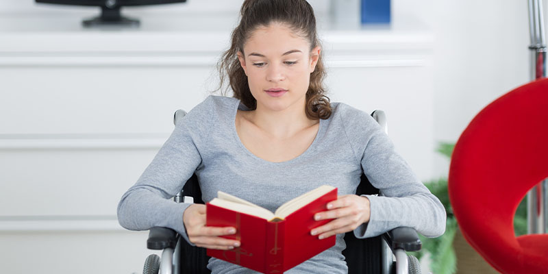 Junge Frau im Rollstuhl liest ein Buch, Link auf Unterseite Vor dem Studium