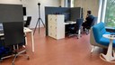 Blick in XSpace Gamelab der Uni Marburg. Ein Mann sitzt an einen von mehreren PC-Plätzen. Daneben steht ein Sofa mit Spielcontrollern. Ebenfalls im Raum steht eine 360° Kamera und eine VR-Brille.