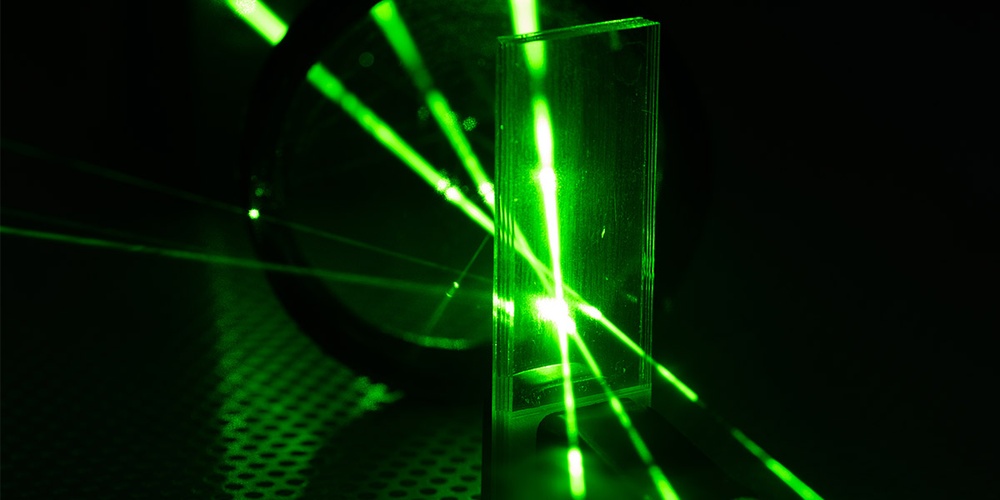 Drei grüne Laserstrahlen laufen in einer Glasscheibe zusammen