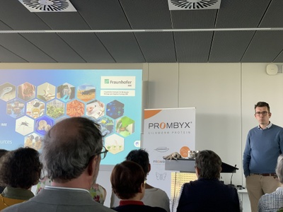 Professor Rühl hält einen Vortrag vor den Alumni, im Hintergrund eine Präsentation zum Aufbau des Fraunhofer Instituts