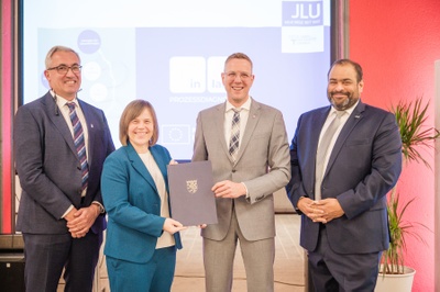 Vier Personen stehen nebeneinander, zwei halten eine Mappe in den Händen.