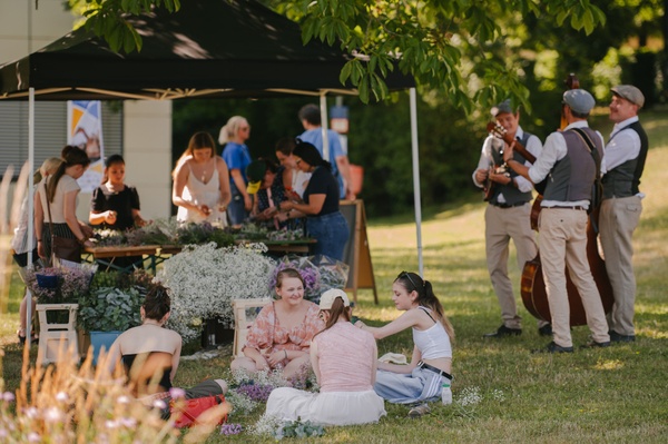 Campus-Picknick_01.jpg Menschen im Gras, die picknicken, im Hintergrund Essensstände und Musiker.