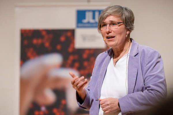 Ringvorlesung Lorenz.jpg Eine Frau mit kurzen grauen Haaren und lila Blazer spricht zu einem nicht sichtbaren Publikum. Im hintergrund steht ein Roll-Up mit JLU-Logo.