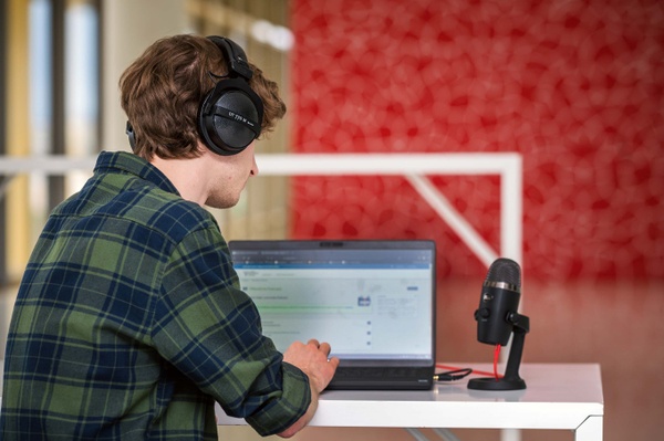 Podcaster Podcast-Aufnahme: JLU-Angehöriger mit Laptop, Kopfhörer und Mikrofon am Tisch