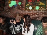 Versuchsbild Vier Personen sitzen in einem Pub an einer Ziegelwand. An der Wand hängen dekorative Schilder, darunter eines mit der Aufschrift „CORK, IRELAND“. Die grünen Kreise auf den oberen Texten symbolisieren die Blickrichtungen der Testpersonen.