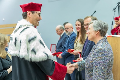 Der Rektor der Universität Lodz in einer traditionellen akademischen oder zeremoniellen Tracht mit weißem Pelzbesatz schüttelt Frau Lorenz in einem gemusterten Blazer die Hand.
