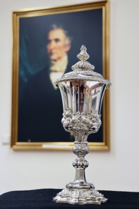 Großaufnahme vom Deckelpokal. Im Hintergrund verschwommen ist das Gemälde von Justus Liebig im Goldrahmen.