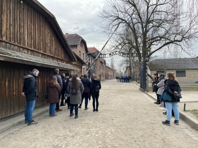 Am Eingang von Auschwitz sieht man links und rechts der Lagerstraße Baracken stehen. Einige Seminarteilnehmende stehen dort und schauen sich alles an.