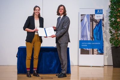 Chistina Mary McCusker (links) hat beim Akademischen Festakt der JLU den DAAD-Preis für ausländische Studierende aus den Händen von Prof. Dr. Alexander Goesmann, Vizepräsident für Wissenschaftliche Infrastruktur, erhalten. Foto: JLU / Katrina Friese