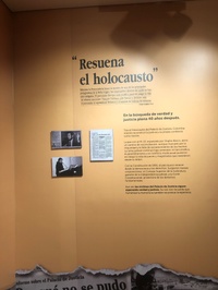 Eine Wand aus der Ausstellung. Sie ist in einem hellen Braun gehalten, darauf drei kleine historische Fotos und spanische Beschreibungstexte.