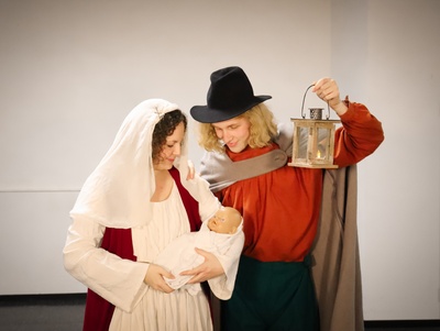 Maria hält eine Babypuppe im Arm. Joseph hält eine Laterne in die Höhe. Beide schauen glücklich auf das Jesuskind.