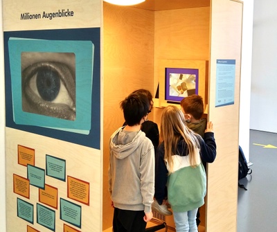 Drei Kinder schauen sich im Mathematikum auf einen Bildschirm an einer Wand.