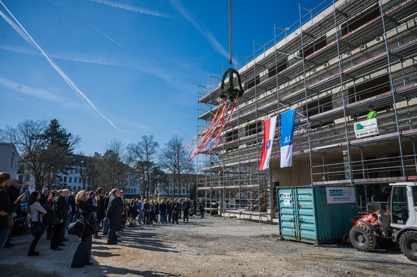 Rohbau mit Flaggen des Landes Hessen und der JLU - im Hintergrund Gäste beim Richtfest des ILH