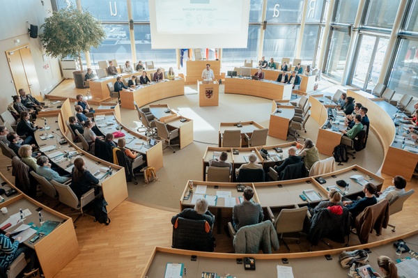Plenarsaal des Rathauses mit Rednerpult und Teilnehmenden auf den Sitzen im Rondell. - Foto: Katrina Friese