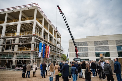 Eine große Gruppe Menschen schaut zu, wie ein Krank einen Richtkranz in die Höhe fährt. Im Hintergrund links der Rohbau des Seminargebäudes. Rechts ein weiteres Uni-Gebäude.