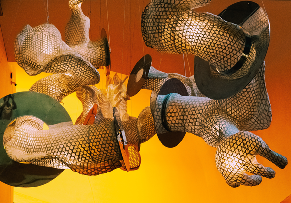 Image of an art installation of fabric-like material in arm- and hand-like shape hanging from the ceiling
