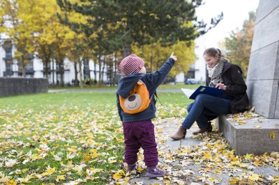 Woman reading a book while a child is playing in autumn leaves