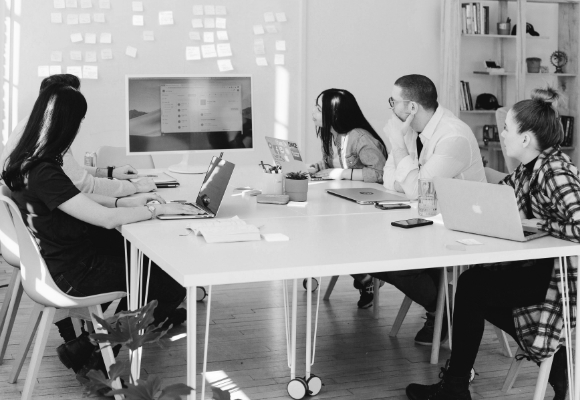 A group of five people is shown sitting at a conference table, looking at a large screen at the end of the table. Click here to be redirected to our event calendar.